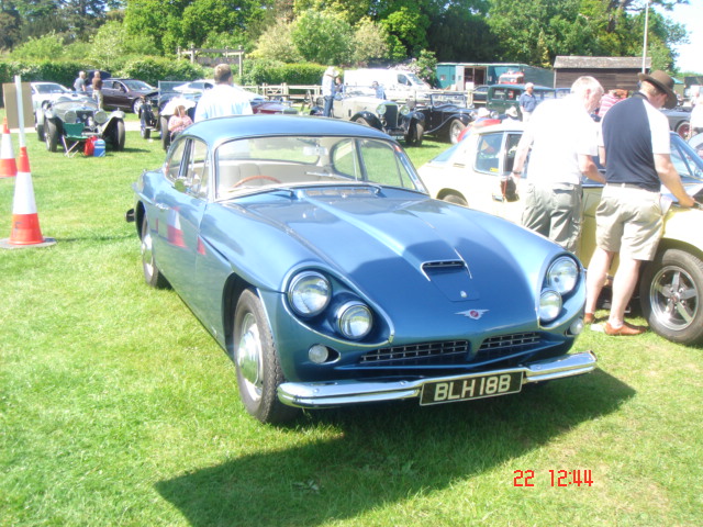 Old Warden car show - Page 1 - Classic Cars and Yesterday's Heroes - PistonHeads - The image captures a vibrant outdoor scene on a lush green field, bathed in sunlight. The main attraction is a vintage blue car with a distinctive handwriting-like text on the front. This car is the centerpiece of the image and is surrounded by a group of people, some of whom appear to be inspecting or admiring it. In the background, there are other cars and trucks which are parked in a line, indicating a possible car show or gathering. The image also contains other cars and flares, adding to the festive atmosphere. The date of the photo is indicated as 22nd February 1944.