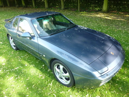 Crunching gears on 944 S2? - Page 1 - Front Engined Porsches - PistonHeads - The image depicts a dark blue or black sports car set against a backdrop of lush green grass and mature trees. The car is positioned slightly to the left, giving a clear view of the vehicle's profile. The sun casts a soft illumination on the car, highlighting the sleek design and glossy finish. The atmosphere is peaceful and serene, suggesting a calm and controlled environment.