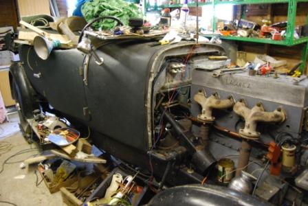 Pistonheads - This image features a vintage vehicle that is in the process of being repaired or restored, possibly in a garage setting. The vehicle appears to be a model with large fenders and a noticeable engine block prominently visible. It is heavily damaged with parts strewn and missing, showing signs of paint stripped off and general disarray, which indicates either extensive wear or intentionally dismantled for restoration.

The engine block and fenders have rusted over time, adding to the distressed aesthetic of the scene. The interior of the vehicle is visible with a combination of exposed metal and enamel surfaces, reflecting the vehicle's antiquated elements.

The overall mood of the image suggests a space dedicated to historical vehicles, with tools and parts scattered around, hinting at ongoing work or research related to automotive history. The focus is on the vehicle, highlighting the intricate details of its design and state of disrepair.