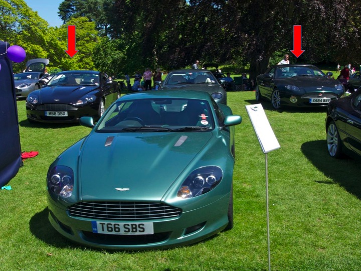 hever pics - Page 1 - Aston Martin - PistonHeads - The image captures an outdoor car show where several cars are exhibited on a grassy field. A green sports car and a black luxury car are among the displayed vehicles, with the green car prominently in the foreground and the black car further away. In the background, there are red squares indicating the presence of markers or boundaries for the exhibition. People can be seen scattered around the field, likely attendees of the event, enhancing the lively atmosphere of the scene. The focus of the image is the group of vehicles displayed, their sleek designs contrasting with the natural backdrop.