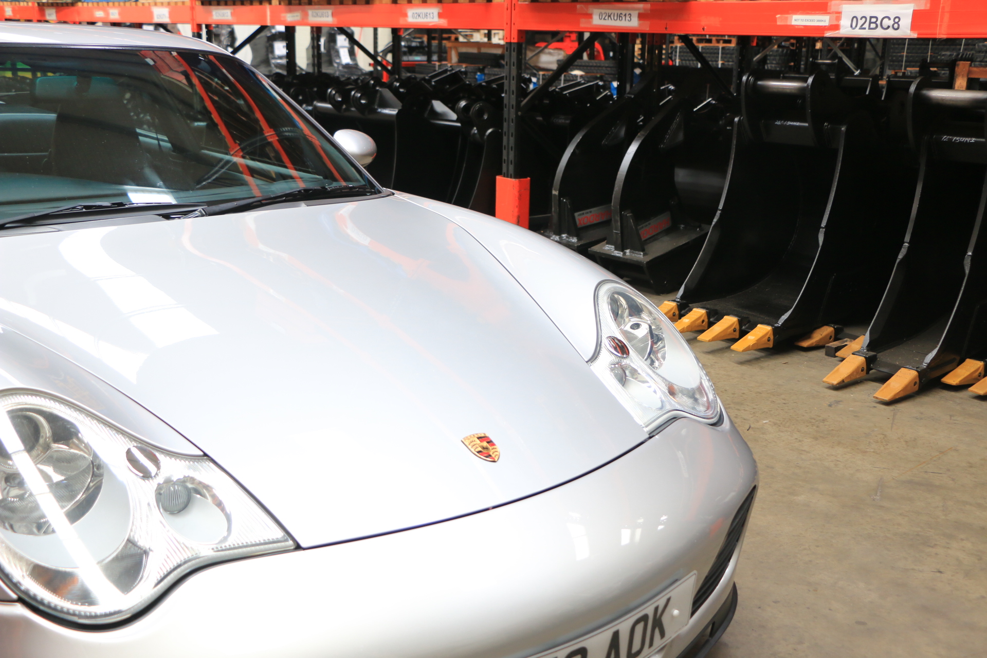 GT2 - Page 140 - Porsche General - PistonHeads - This image features a white Porsche car parked on a floor inside a building. The car is facing the front left side of the image. Behind the car, there are rows of vehicle ramps, each leading to a gantry supporting another ramp, suggesting a professional car dealership setting. The image is well-lit and clearly focuses on the car, with the ramps in the background out of focus. There is no text visible in the image.