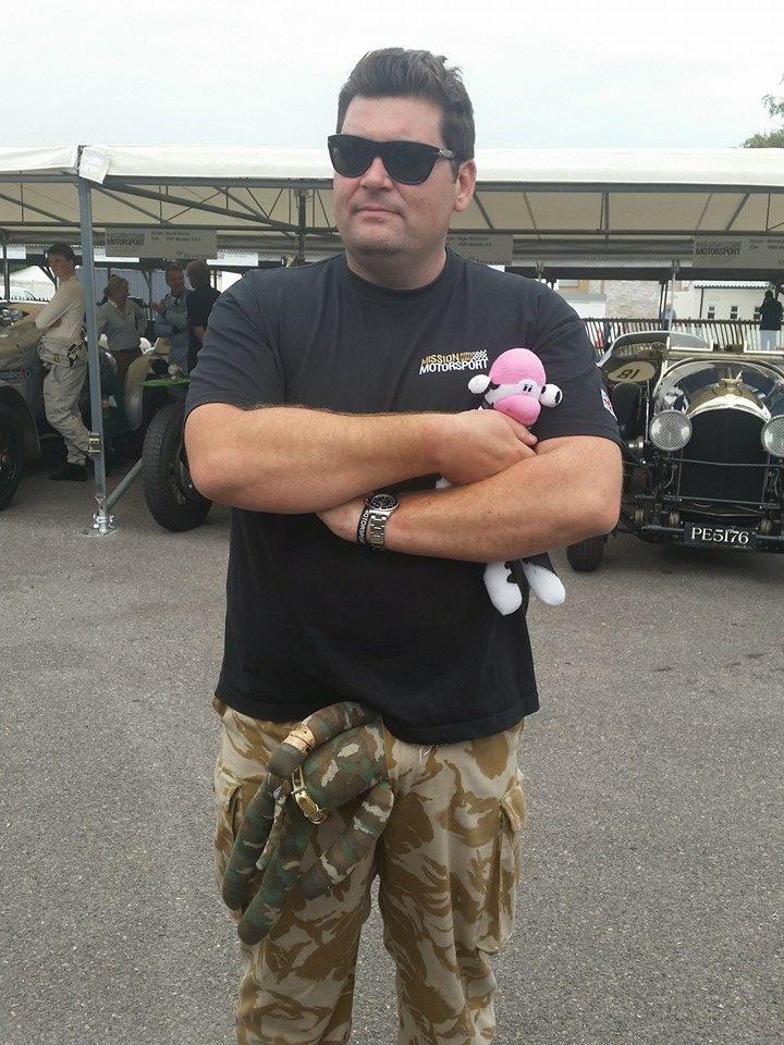 Has there ever been a PHers mugshot thread?  A new line up - Page 3 - The Lounge - PistonHeads - The image is a photograph of an adult male with a casual, relaxed pose. He is wearing sunglasses, a black t-shirt, patterned shorts, and is holding a small, pink plush toy with both hands. His dark hair is slightly tousled, and he appears to be indoors, with other individuals and equipment visible behind him. The overall atmosphere is casual and friendly, possibly of a social gathering or event of some kind.