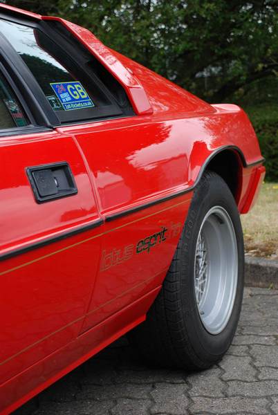 Service Pistonheads Sunday - The image showcases the left side of a red sports car, focusing on its rear tire and wheel. The car is parked on a street, and the tire is prominently visible with the words "spirit" and "goodyear" visible on it. A sticker can be seen in the side window, likely indicating some form of identification or affiliation. The environment suggests that the car is stationary, as there's no indication of movement.