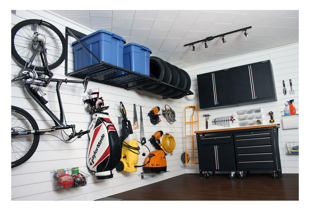 Our build thread, renovation and extension - Page 109 - Homes, Gardens and DIY - PistonHeads - This image depicts an organized garage with a strong emphasis on storage and crafting equipment. The walls are white with horizontal wood paneling and there are black shelves stocked with tools and supplies. Costumes hanging from hooks suggest this space might be used for hobbies or creative activities. Bicycles are leaning against the wall, and stairs can be seen in the corner, indicating that there might be more levels to this space.