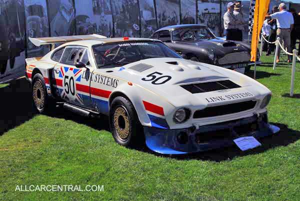 70's DBS question; - Page 1 - Aston Martin - PistonHeads - The image depicts a classic Jensen Link System sports car on display at a car show. The car is painted in a striking red, white, and blue color scheme, highlighting a design that is both vintage and race-inspired. Its sleek body and prominent spoiler are distinct features of this vehicle. In the background, other classic cars can be seen, adding to the atmosphere of the event. The word "ALLCARCENTRAL.COM" is visible, suggesting a source of information about this and related events. This scene captures the essence of automotive history and enthusiast gatherings.