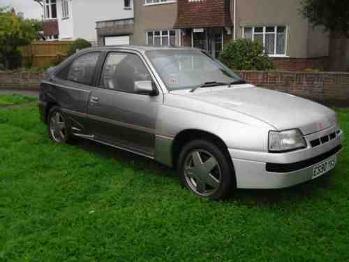 Pistonheads - The image shows a silver, two-door hatchback car parked on grass in front of a house. The car appears to be an older model, possibly a late 1990s or early 2000s vehicle, with visible alloy wheels and a distinctive front design with angled headlights and a large, rectangular grille that includes a logo at the center. The car is parked during the day under overcast or cloudy sky, and its general condition suggests it may have been used for an extended period. The green lawn and the residential structure in the background suggest a suburban setting.