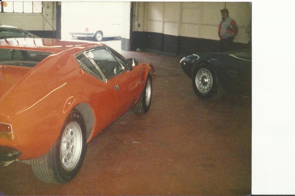 Anyone remember Pullicino Classics? - Page 4 - Supercar General - PistonHeads - The image captures a scene in a spacious garage. The dominant vehicle is an orange sports car, featuring a convertible top and sleek, metal body. It's parked alongside another vehicle; a dark-colored sports car with eagle insignia, indicating it might be an American muscle car. In the background, there's a man with a red and gray jacket standing next to a white car, possibly overseeing the garage or the vehicles. The image has a vintage feel, suggesting it may have been taken several years ago.