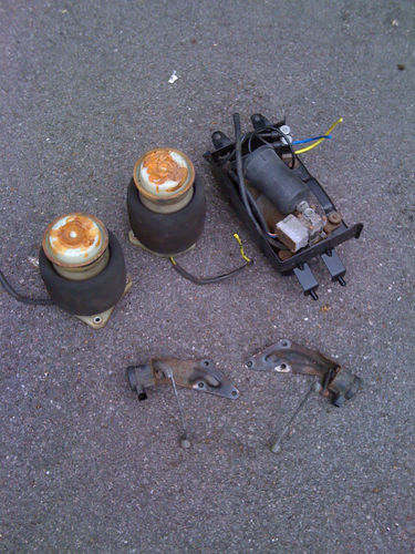 How does Vito rear air suspension work? For my Jeep!!?? - Page 1 - Mercedes - PistonHeads - The image depicts a set of automotive anti-lock braking system (ABS) parts laid out on a paved surface. There are three main components: a power supply unit, two tone rings attached to brake pads, and a fractured brake sensor unit. The components appear used and possibly damaged, indicating that they may have been removed from a vehicle. The coloration suggests they are made from metal and rubber. The positioning of the items suggests someone might be in the midst of inspecting or disposing of these parts. The overall setting appears to be an outdoor location, such as a parking lot or driveway.