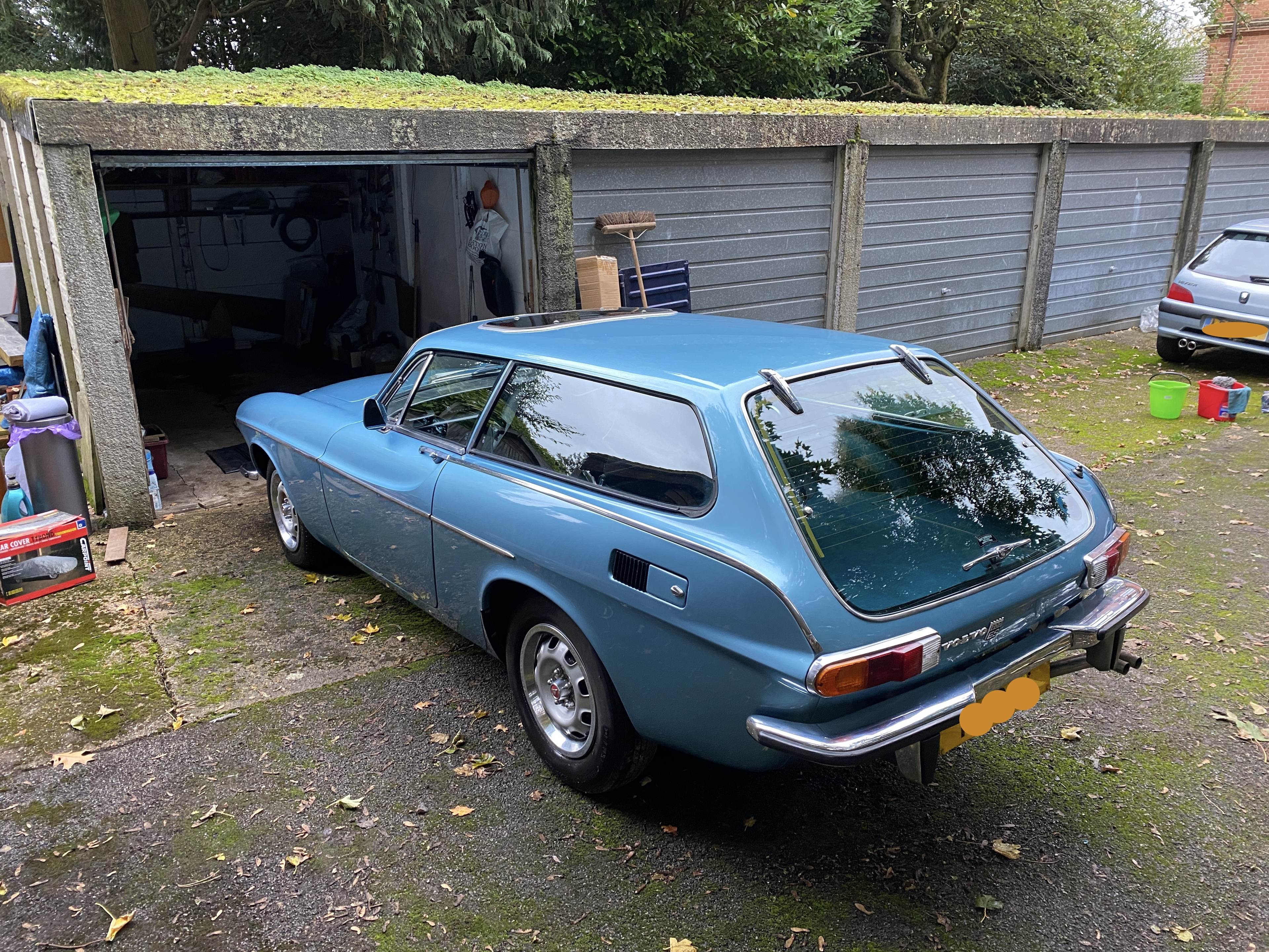 Recommissioning a barn find Volvo P1800ES - Page 3 - Readers' Cars - PistonHeads - The image shows a classic car parked inside a garage. The car is an older model, reminiscent of the 1960s or 1970s, with a distinctive teal color and white stripes on the hood. It has a European-style license plate. The car's design includes round headlights and tail lights, which are characteristic features of vintage cars. The garage has an open door, revealing the interior is well-lit and seems to be used for vehicle storage and maintenance.