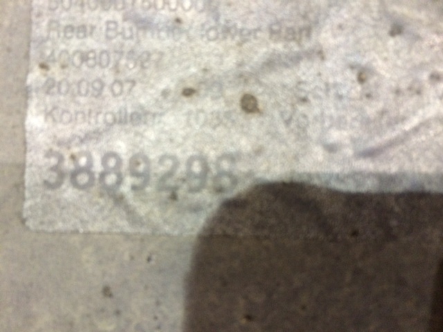 A brown teddy bear sitting on top of a rock - Pistonheads - The image shows a close-up view of a metallic surface that appears to be scratched and slightly dented. On this surface, there's a peeling label with numbers and letters, suggesting some form of identification. The barcode and serial number indicate that this might be a part from an appliance or a type of equipment where such tracking numbers are used. The focus is sharp in the center of the label, but the edges of the peeling label are blurred, making it slightly difficult to read the text. The overall condition of the surface also implies that the item has been used or handled roughly.