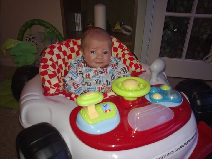 Can you photoshop my friends baby into an F1 car please? - Page 1 - General Gassing - PistonHeads - This image captures a young child sitting in a red and white toy car. The baby is dressed in a dark-colored outfit. The car is topped with a canopy, providing a sense of enclosure and safety for the child. The backdrop is rather nondescript, focusing the viewer's attention on the child and the toy car.