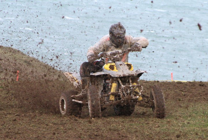 Quad for farm - Page 1 - Off Road - PistonHeads - In the image, a person is riding a four-wheeler through a muddy field. The four-wheeler is kicking up clouds of dirt and mud as it moves, which adds to the dynamic feel of the scene. The rider is dressed in weather-appropriate clothing, indicating it might be a cool or wet day. In the background, there is water, implying that the field is near a body of water. The entire scene portrays a thrilling outdoor sport or recreational activity.