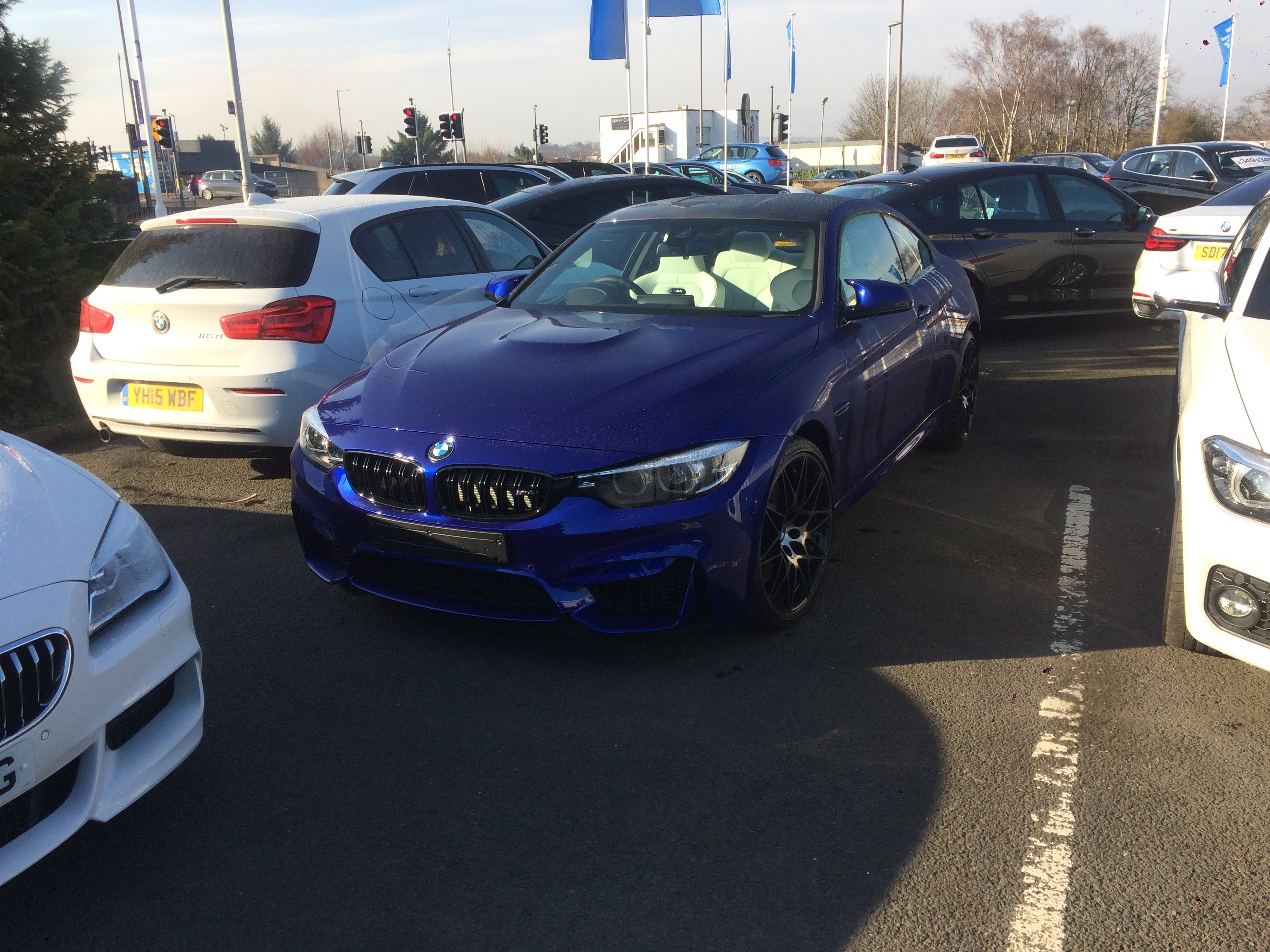 Just bought an M6 Gran Coupe - Page 24 - M Power - PistonHeads UK - The image depicts a scene in a parking lot. In the foreground, there's a striking blue BMW car with unique customizations such as aftermarket wheels and a wide-body kit. This sports car is parked among other cars that are more standard in design. The background shows the expansive surface of the parking lot, with a few traffic lights visible at the far end. Above, the sky appears overcast, suggesting it might be a cool or cloudy day. The overall impression is one of a casual gathering of car enthusiasts, perhaps at a car show or similar event.