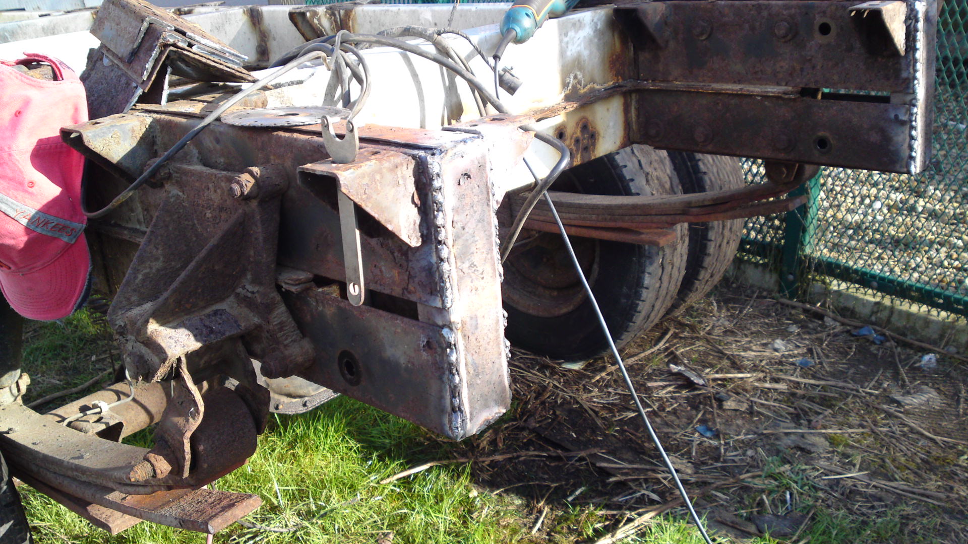 Transporter bed fabrication. - Page 4 - Commercial Break - PistonHeads - The image shows a metal structure, likely a piece of machinery or equipment, sitting on the ground which appears to be in an outdoor, possibly rural setting. The structure is comprised of various steel components, including a large metal frame and several rusted parts. It's surrounded by a grassy area with some scattered leaves, indicating an abandoned or neglected state. The presence of a pink object near the equipment, possibly a tag or identification label, stands out against the metallic parts. The structure seems to be in a disconnected or inoperable condition.