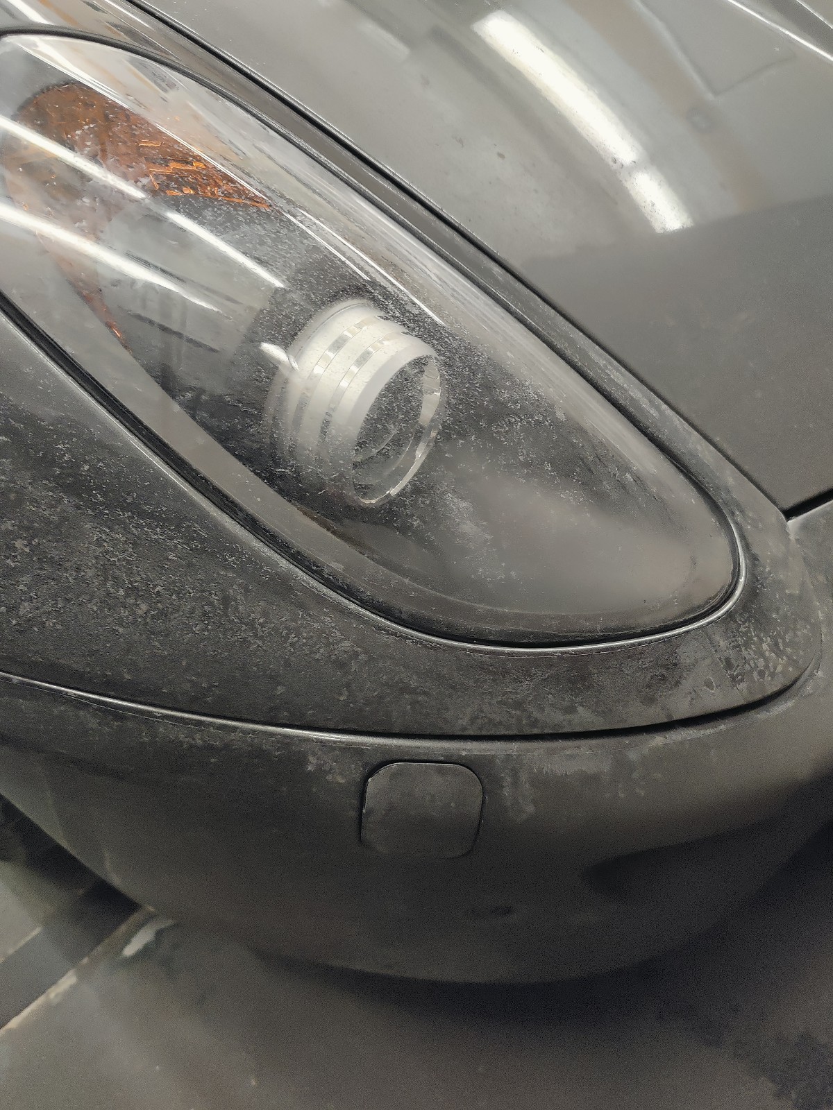 A close up of a parking meter on a city street - Pistonheads - The image shows a close-up view of the front part of a sports car, specifically focusing on the headlight area. The headlights are off, and there's visible dust or dirt on the surface, suggesting it might be a new or recently used vehicle. The background is dark and out of focus, emphasizing the car in the foreground. It appears to be taken indoors as indicated by the reflective floor. The vehicle has a sleek design typical of high-performance sports cars, and its front bumper is visible, showing some minor wear or scratches.