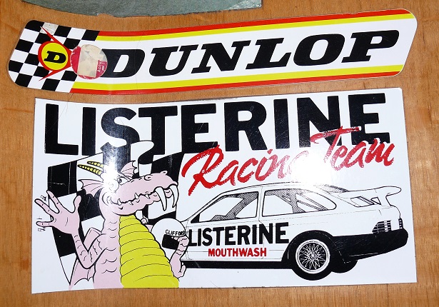 Show Us Your Stickers! - Page 1 - Formula 1 - PistonHeads - The image showcases a collection of two car bumpers, both bearing distinctive brand names. One bumper prominently displays the "Listerine" logo along with a unique illustration of a dragon hitchhiking a ride in a car, humorously conveying "Mouthwash". The other bumper prominently displays the "DUNLOP" logo, indicating the brand of the tires produced by the company. Both bumpers draw attention with their bold colors and visible brand logos, suggesting that they are promotional items or products related to automotive and personal care.