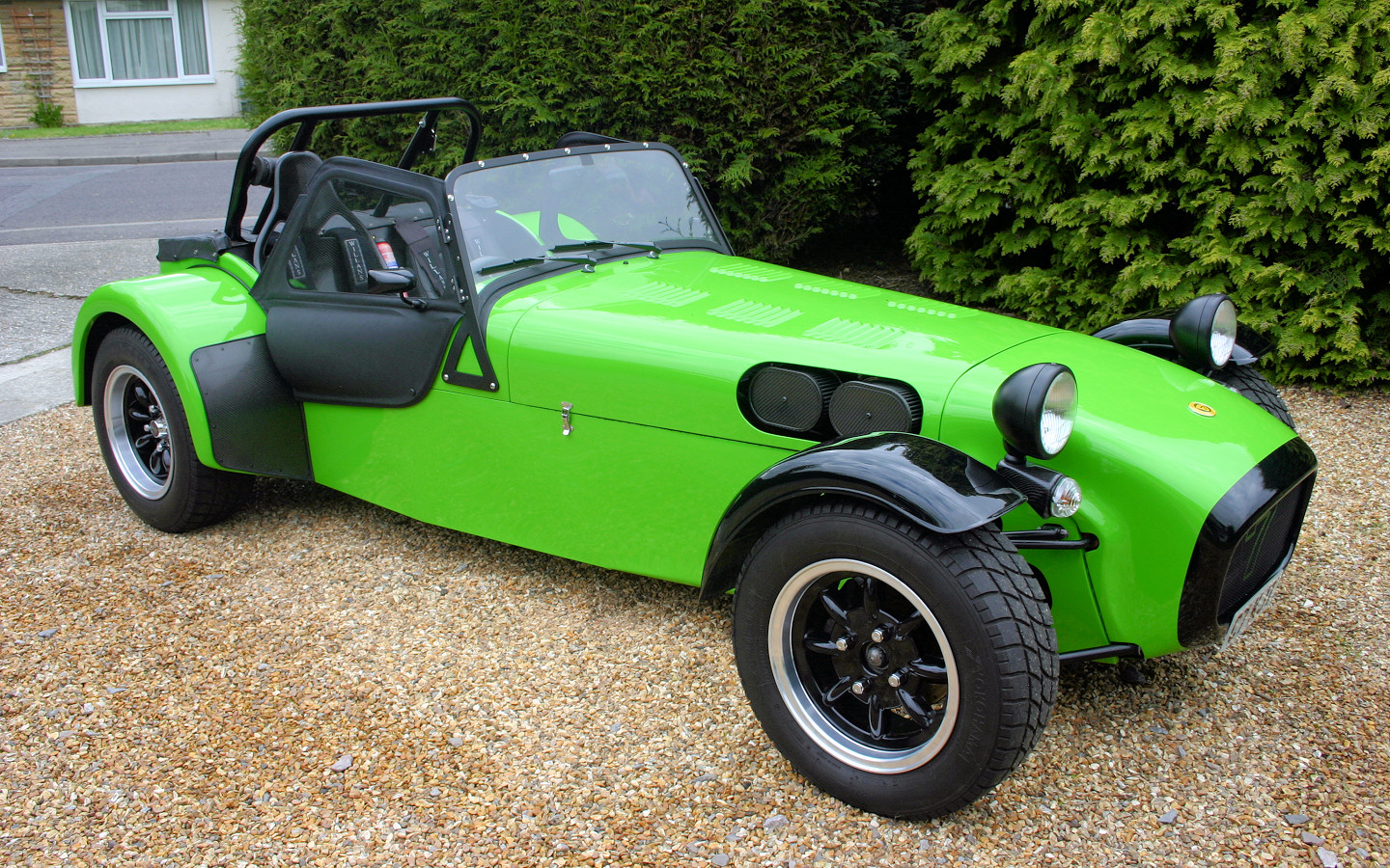 Not enough pictures on this forum - Page 4 - Caterham - PistonHeads - The image shows a striking green vintage race car parked on a gravel driveway. The car's sleek design is accentuated by its large black wheels and custom touches like a roll bar inside. The vehicle features a prominent front grille and round headlights, giving it a unique and classic appearance. The car's vintage appeal and vibrant green color make it a standout on the gravel driveway.