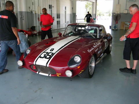 Pistonheads Sepang Afos - The image captures a scene inside a garage where four men are gathered around a classic sports car painted in a striking combination of red and white with black stripes. The car's number, "38," is prominently displayed on the side. One man, wearing a black shirt, is examining the open hood of the vehicle, revealing the engine and its intricate details. Another man, dressed in a red shirt and black pants, stands near the car, perhaps observing the engine or considering the artful aerodynamic body design. On either side of the car, two more men can be seen, one of them wearing a red shirt, and the other in a black shirt. This convivial gathering appears to revolve around the shared appreciation for the classic sports car.