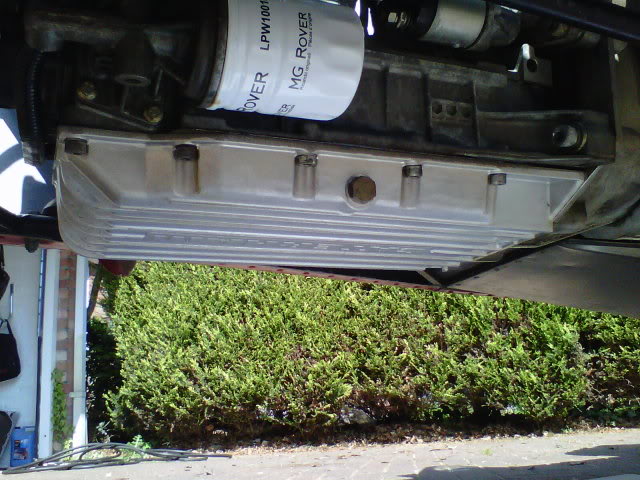 Pistonheads - The image shows a close-up of an automobile's mechanical underbody. We can see some components from the suspension system and parts of the engine, including an air intake piping system. The engine is not visible; only the underside of it is seen. Below the vehicle, there is a bush with lush green leaves, indicative of a well-kept garden or a plant growing in a trimmed lawn. The focus of the image is on the engine bay and its surrounding areas rather than the ground below.