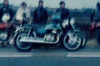 Show your 70's bike... - Page 1 - Biker Banter - PistonHeads - The image is a grainy, vintage-looking photograph capturing a group of people sitting on motorcycles. There are several individuals present, each with their distinctive style. The foreground features a prominently centred motorcycle, while others are scattered in the background. The setting appears to be an outdoor space, possibly near a body of water, as indicated by the presence of a waterway in the background.