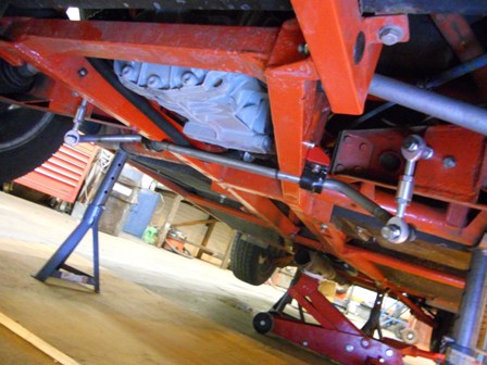 A red and black motorcycle parked in a garage - Pistonheads - The image shows a close-up view of the underside of a vehicle, likely focusing on the suspension system and the area around one of the wheels. The suspension components are typically made of metal and rubber, with visible shocks and struts. The wheel well appears to be red and is a common color for that part of a vehicle. The background is indistinct but looks like a warehouse or a shop floor, with industrial elements and equipment. There are no visible people or activities in the image, suggesting a still image with a focus on the mechanical components of the vehicle rather than the surrounding environment.