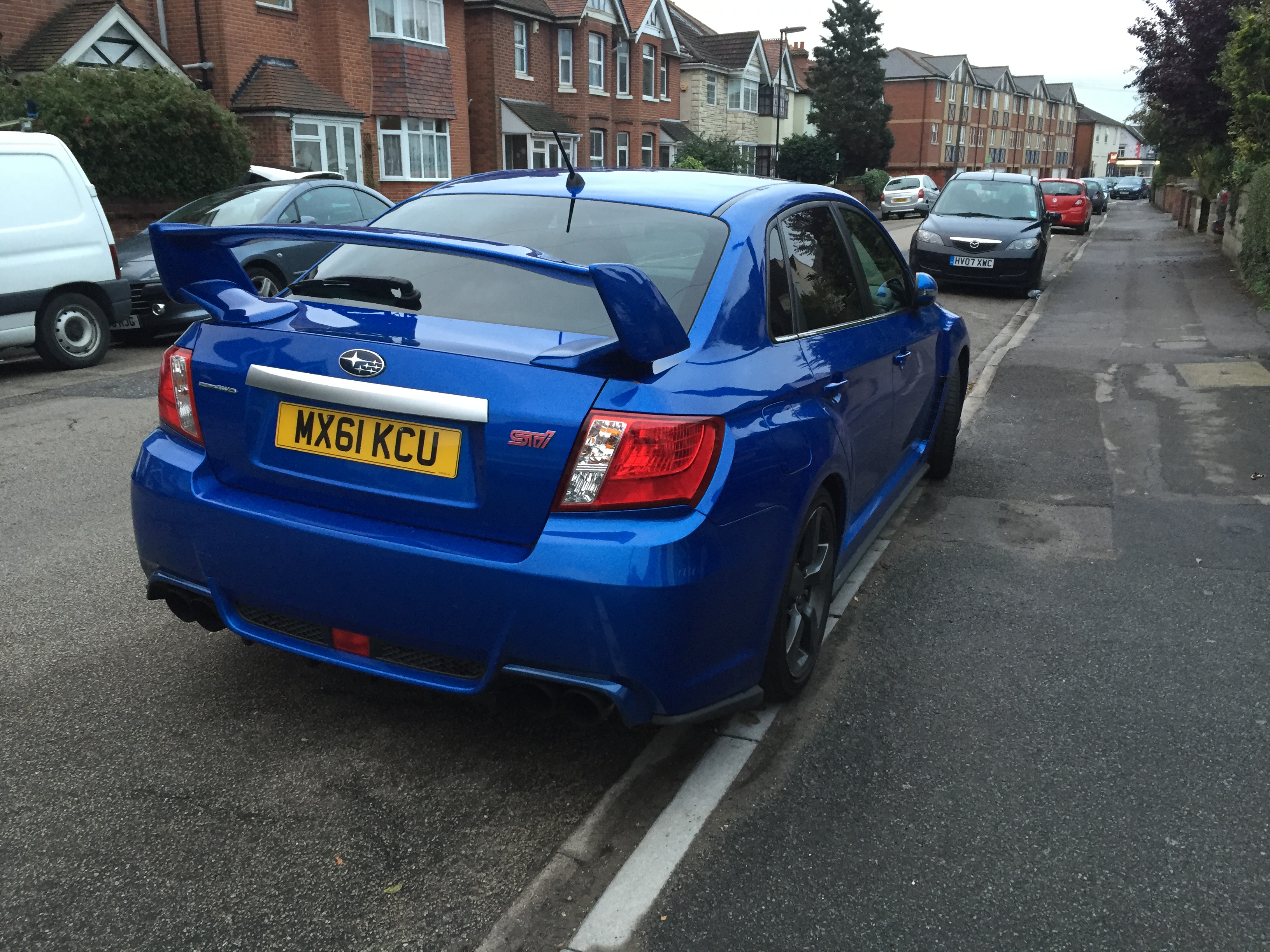 RE: Goodbye STI - Subaru calls time on the WRX - Page 10 - General Gassing - PistonHeads - The image shows a blue Toyota car parked on the side of a street. The car is positioned in front of a building, and it has a spoiler on the rear of the car. In the background, there are houses and other cars parked behind the Toyota. The street appears to be quiet and residential, and the environment suggests it might be early in the day due to the soft lighting.