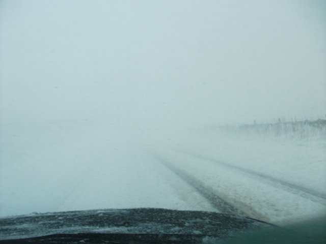 9-3 Aero TTiD - Page 1 - Saab - PistonHeads - The image presents a misty and snowy day, likely a dawn or dusk due to the muted light. The sky forms a backdrop that is reduced to a soft and widespread blur, contributing to the atmosphere of coldness and isolation. The wet road appears glossy, indicating recent road usage that has since been covered by fresh snowfall. The road cuts through the landscape, guiding the viewer towards an obscured point in the distance, suggesting travel or a journey amidst the winter weather.