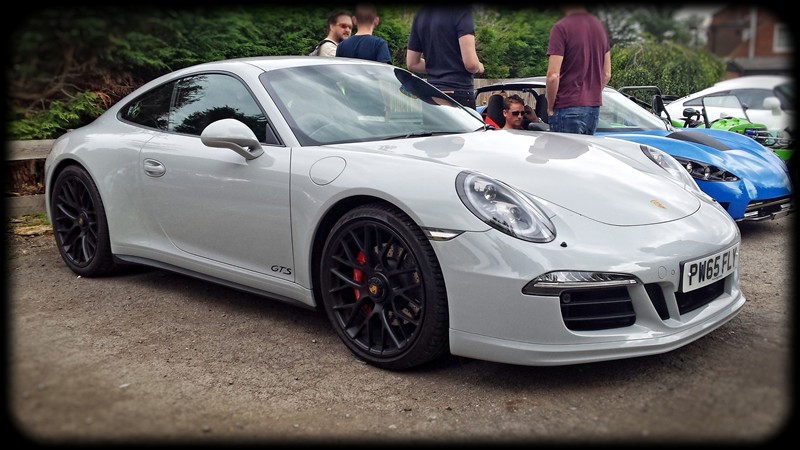 Bucks Cars & Coffee - Page 4 - Herts, Beds, Bucks & Cambs - PistonHeads - This image features a silver Porsche parked amidst other cars on what appears to be a lot or parking area. The Porsche prominently displays the vehicle's number and brand logo. It is characterized by its iconic design elements such as prominent air intakes and racing-style wheels. The car is parked in what seems to be a public outdoor setting with greenery, and there are other people and vehicles present, implying a casual, social gathering.