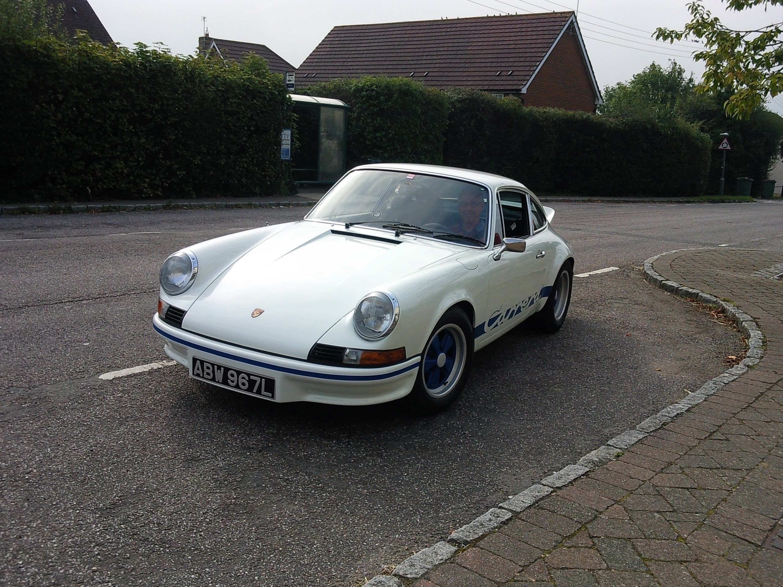 COOL CLASSIC CAR SPOTTERS POST!!! Vol 2 - Page 86 - Classic Cars and Yesterday's Heroes - PistonHeads - The image shows a vintage Porsche 911 parked on a street. It's a sunny day, and the car's color is solid, white or black, depending on lighting. The car is equipped with alloy wheels, and it appears to be in good condition, maintaining its classic appearance. The street is lined with brick pavers and houses can be seen in the background.