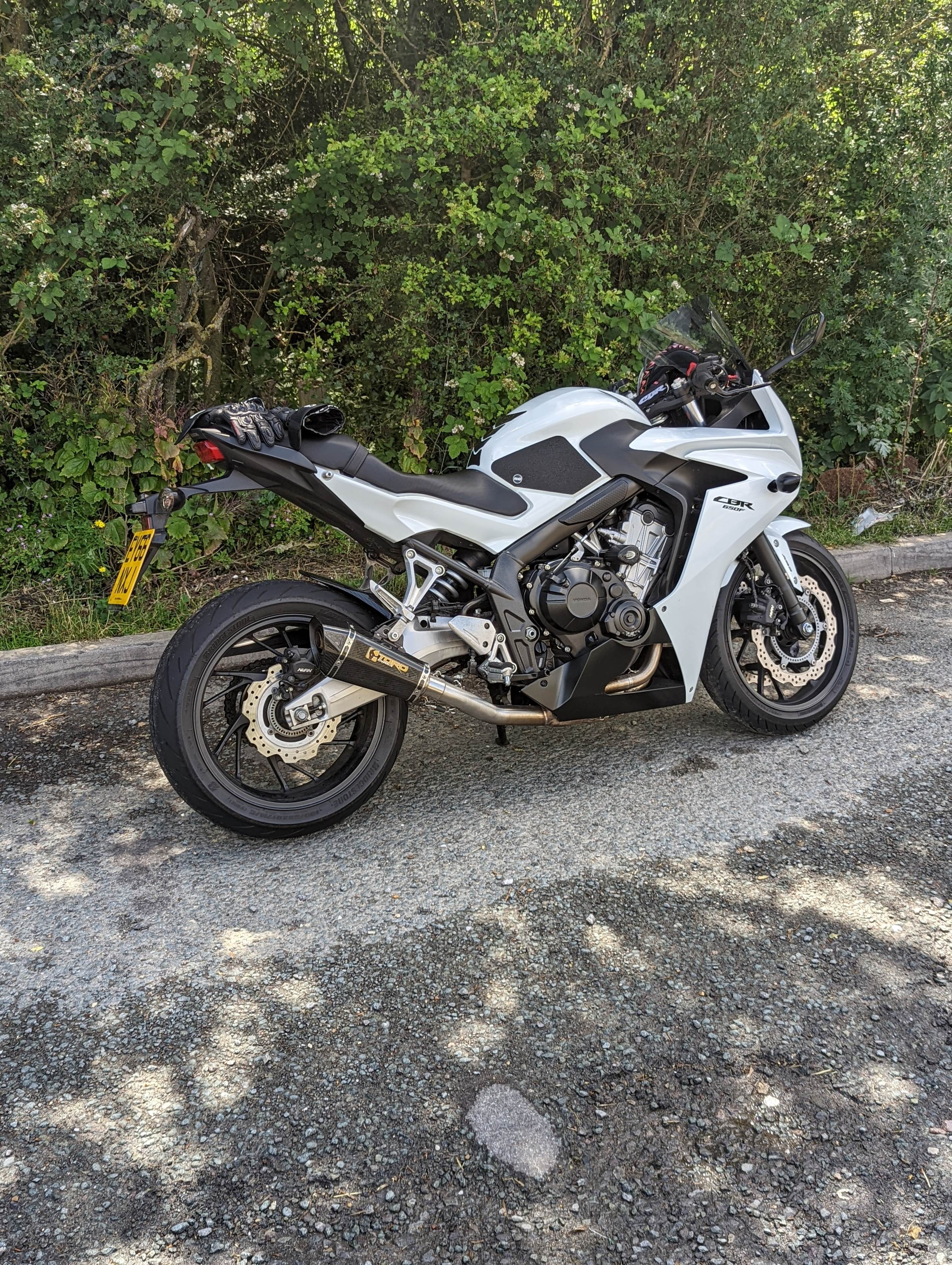 A picture a day...biker banter (Vol 6) - Page 134 - Biker Banter - PistonHeads UK - The image shows a motorcycle parked on the side of a road. The bike is white and black, with the engine visible at the front. It has a sporty design, indicated by its aerodynamic fairings and sharp angles. In the background, there are trees, suggesting that the location might be in a rural or suburban area. Additionally, there's a small sign visible, but it's not clear what it says. The sky appears to be overcast, with no distinctive landmarks or other objects of note in the immediate vicinity. The photo is taken during the daytime under natural lighting conditions.