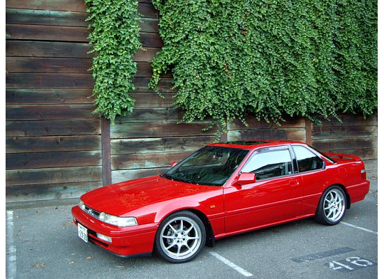 A red car parked in front of a red fire hydrant - Pistonheads - The image features an old-looking red Toyota Corona parked against a wooden fence. The car is two-door, and its red exterior appears to be in good condition. The wooden fence in the background has ivy growing over it and is made of dark-colored wooden planks. Also worth noting is a parking spot marker with the number 48 in the bottom right corner of the image.