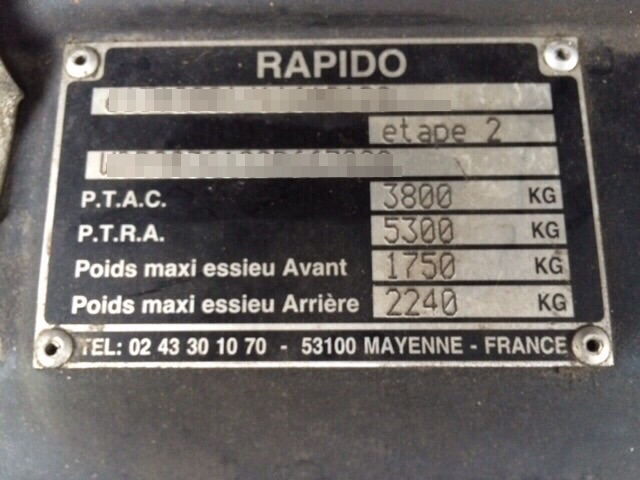 A close up of a street sign with a sky background - Pistonheads - The image features a black label on the front of an assembly component with French text and numbers. It displays product information such as part numbers, weights, dimensions, and quantities for kilograms and grams of a product named "RAPIDO," though the full name is obscured by the orientation of the photo. There is an indication of a specific model from P.T.A.C. with part numbers 3800 and 5300. The text also includes references to the material composition and responsibility. The label provides contact and tracking information including a Tel number and a serial number for the part.