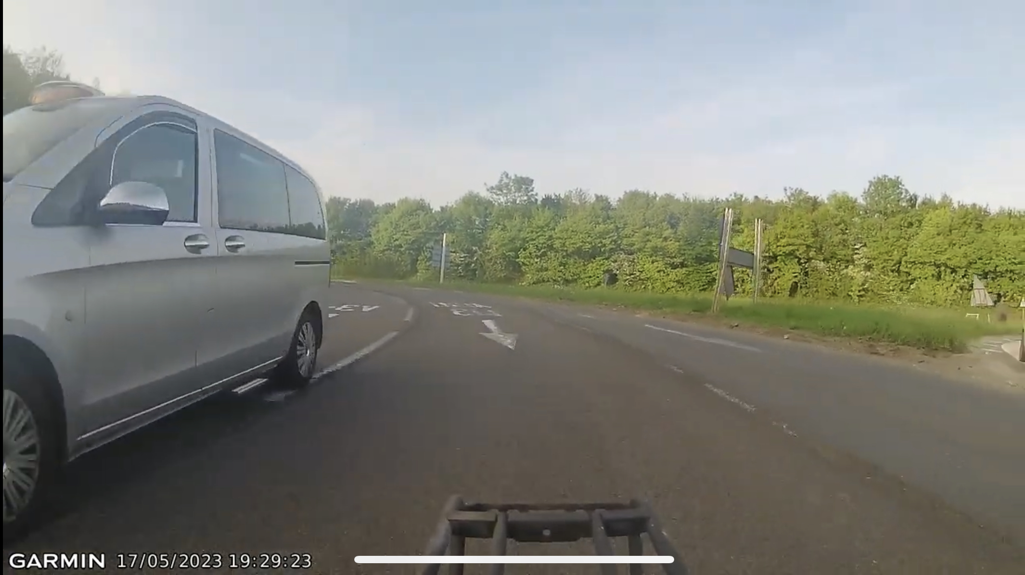 The image shows a screenshot of a car dashcam that captures the interior view of a vehicle and its surroundings. It appears to be a clear day with blue skies. On the road ahead, there's a silver car in front of the vehicle recording the scene, and to the right, there is a white van. The dashboard of the vehicle is visible, showing a GPS system indicating it's on a highway named 'Garmin'. There are no people visible in the image.