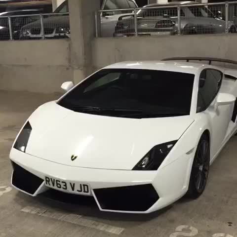 A white car parked next to a parking meter - Pistonheads - This image features a white Lamborghini sports car with a sleek design, set against a background that includes a concrete surface and the partial view of a parking garage. The car's top is slightly visible, revealing its convertible feature. Other vehicles are parked in the background, but the Lamborghini is the main focus. The white color of the car contrasts with the darker tones of the surroundings.