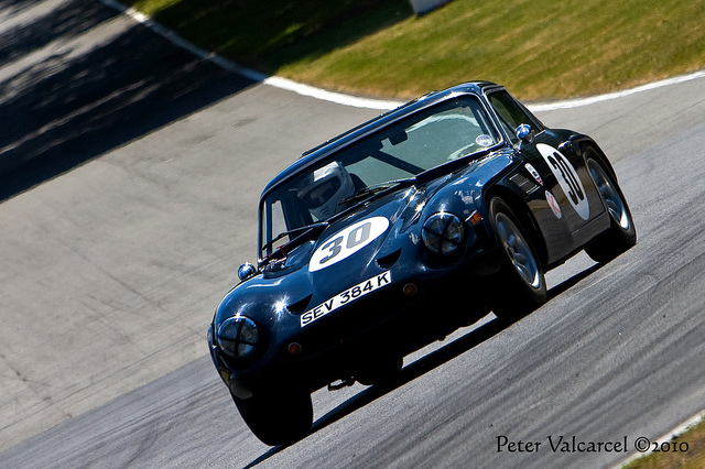 Right Hand Drive 2500s - Page 1 - Classics - PistonHeads - The image captures a vintage racing car, numbered 30, on a race track during what seems to be a competition or track day event. The car is a dark blue with the number 30 prominently displayed on both the hood and the side, along with the registration number "S3V 384K." It's designed for classic racing, possibly reminiscent of the 1950s or 1960s, with a prominent front grille, aerodynamic proportions, and a driver wearing a racing suit, indicating competitive racing. The track has a wide curve in the background, suggesting that the car is either negotiating a tight corner or approaching the upper part of the track. The shadows cast on the track surface indicate that the photo was taken during daylight on an overcast or cloudy day.