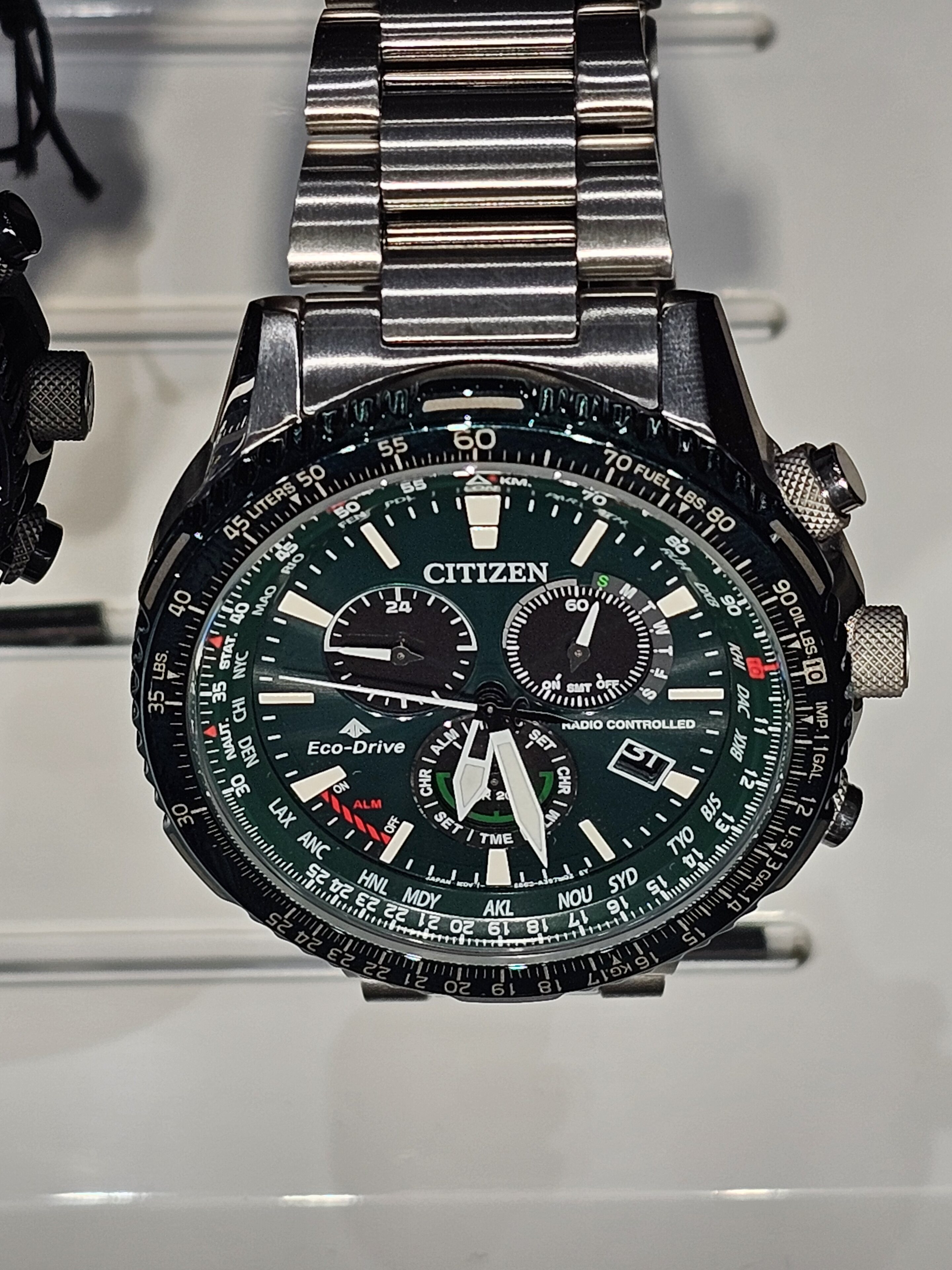 Pistonheads - The image showcases a wristwatch with a green and black color scheme. It has multiple dials and sub-dials, indicative of various timekeeping features. The watch is mounted on a display stand inside a store or exhibition space. In the background, there's a glimpse of another item, possibly another watch or a piece of jewelry. The image does not provide any text or additional context about the location or brand of the watch.