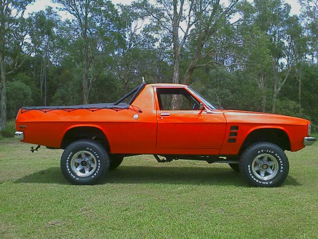 Recommend me a ute..... - Page 1 - Australia - PistonHeads - The image displays a vintage truck painted in a vibrant shade of orange. It appears to be a four-wheel-drive vehicle with a prominent roof rack. The truck sits on grass, and there is a line of trees in the background. The weather seems clear, with no visible signs of rain or overcast skies. The overall scene conveys a sense of strength and color contrasting with the natural surroundings.