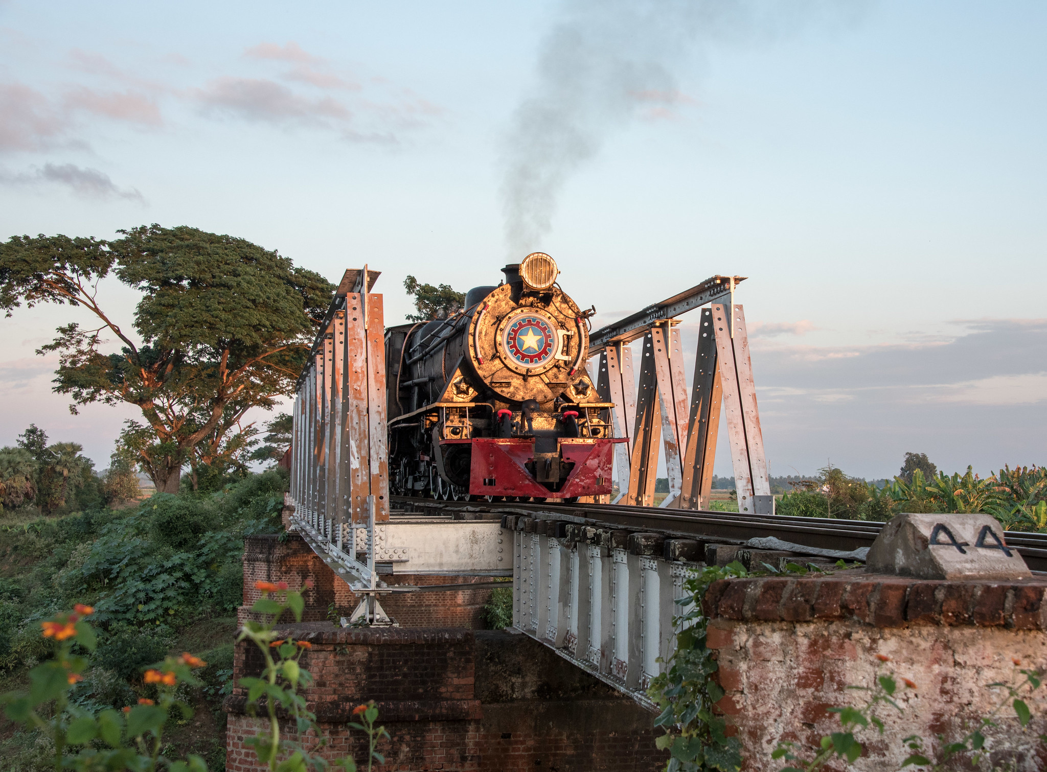 Pistonheads - The image showcases a captivating scene of a train journey. A black locomotive with a yellow stripe is traveling on tracks over a bridge. The bridge, with its sturdy structure, spans the width of a river, providing a path for the train to cross. 

The train, appearing as a small toy-like model in comparison to the vast expanse around it, adds a sense of scale and wonder to the scene. It's journeying through a lush green landscape under a clear blue sky, adding vibrant colors to the image. 

The photo is taken from a distance, providing an overview of the train and its surroundings. This perspective allows for a comprehensive view of the entire bridge and the surrounding environment, emphasizing the isolation of the train's journey. Despite the absence of people in the image, one can almost hear the chugging sound of the locomotive on its tracks. 

The image evokes a sense of nostalgia and adventure, capturing a moment in time as this old-fashioned steam engine makes its way across the bridge. It's a testament to human ingenuity, showcasing how we've conquered nature with our technological advancements.