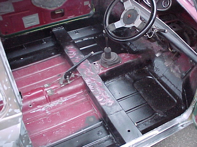 Pistonheads Purchase Advice - The image presents an interior view of a vehicle that appears to be in a scrapyard environment. The interior is predominantly a display of various mechanical components, and the fine details visible show a stage of disassembly. The driver's side door is open, leading the eye towards the exposure of parts typically hidden from view. The handbrake is visible in the center, although the steering wheel is not in view. The components are set against the backdrop of a mock car external structure, painted in a faded red color. The image provides a glimpse into the behind-the-scenes workings of a car scrapyard.