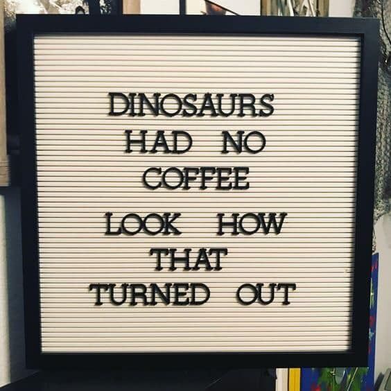 A close up of a sign on a pole - The image features a square frame containing a black background with white lettering. The text on the sign reads "DINOSAURS HAD NO COFFEE LOOK HOW THAT TURNED OUT". This suggests that the message is a playful or humorous commentary, possibly referring to dinosaurs' non-existent coffee consumption and the consequences of this lack, humorously implied by the phrase 'that turned out'. The style of the image appears to be casual, possibly intended for display on a wall or as a decorative piece.