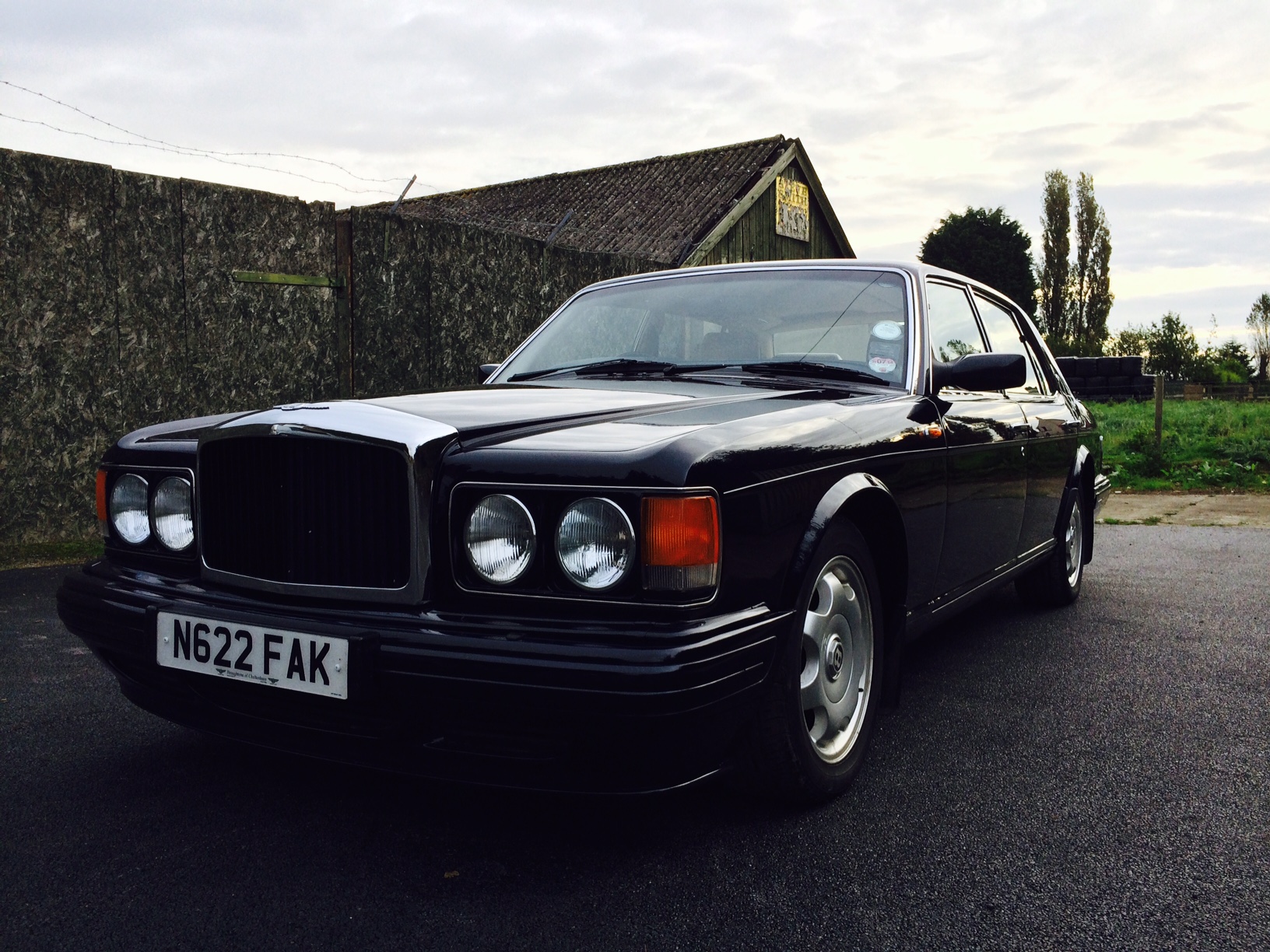 Lets see a picture of your classic(s) - Page 234 - Classic Cars and Yesterday's Heroes - PistonHeads - The image showcases a sleek, black Audi car parked on a paved area. The car sports a prominent front grille and shows signs of a well-maintained vehicle. A garage with a wooden roof can be seen in the background. The sky overhead is filled with clouds, indicating an overcast day. The overall scene suggests a suburban setting.