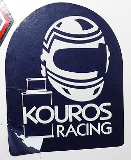 Show Us Your Stickers! - Page 1 - Formula 1 - PistonHeads - The image features a decal or sticker with a logo for "Kouros Racing." At the center of the image is an outline of a racing helmet, accompanied by text at the bottom that reads "Kouros Racing." The logo is applied to the front of what appears to be a vacuum cleaner case, situated on a white surface. The style of the image suggests a brand affiliation or ownership, potentially for a racing-related vacuum cleaner product line. The overall aesthetic of the image is clean and minimalistic.