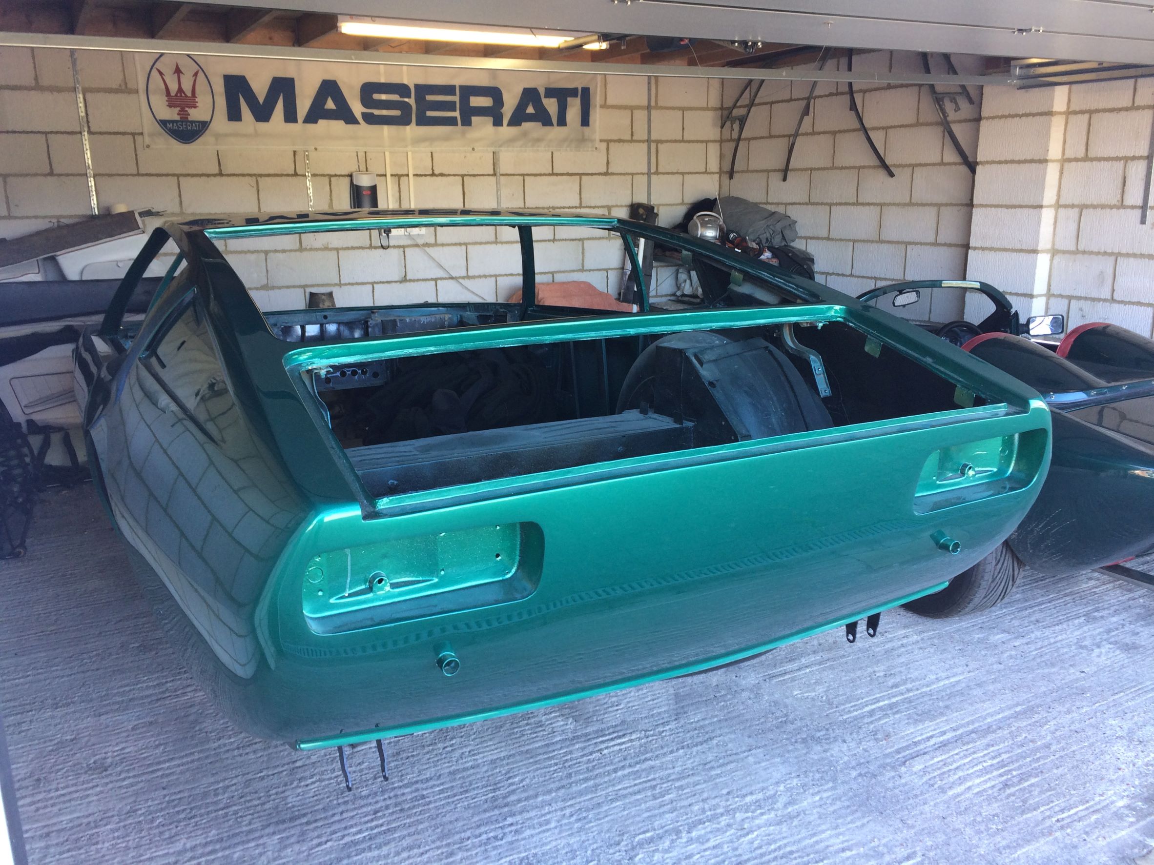 1969 Maserati Ghibli - The Resurection - Page 32 - Classic Cars and Yesterday's Heroes - PistonHeads UK - The image shows a green car parked indoors, likely in a garage. It appears to be a modified or custom vehicle, given the visible modifications and the unique bodywork. The car is not fully assembled; several parts are missing, such as doors and possibly windows. The interior of the car is also visible, revealing a driver's seat. In the background, there's an open door to another room, which partially reveals a second vehicle, although it's not the focus of the image.