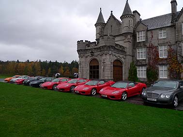 Pistonheads - The image shows a large collection of sports cars parked in front of a majestic castle-like building. The cars are all positioned facing the same direction, suggesting they might be a part of an exclusive gathering or exhibition. The cars are a mix of red and black, adding a vibrant touch to the scene. The building in the background exudes a medieval charm, with its imposing stone structure and multiple turrets. The combination of the cars and the grand building create a picturesque setting.