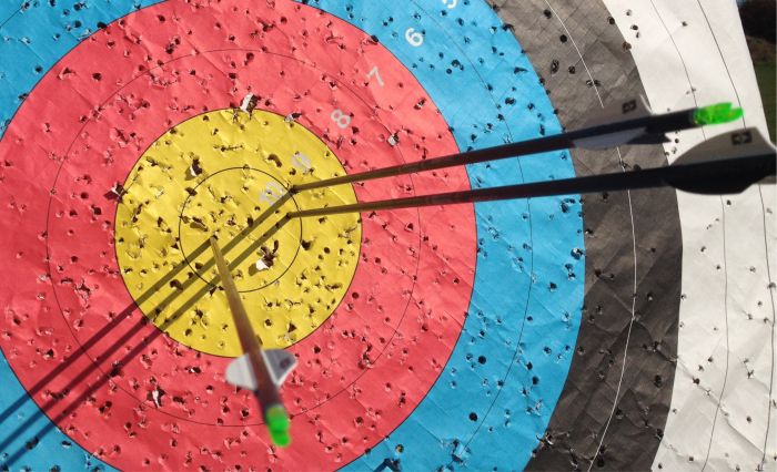 A colorful umbrella sitting on top of a table - Pistonheads - The image showcases a target shooting game in progress. On the circular target, there are multiple holes with fewer holes within the yellow ring and the least number within the red ring, indicating varying degrees of accuracy. A pair of arrows, one green and one white, are sticking out of the target, suggesting that they were used to shoot. The target is hung on a range marked with black and blue lines, and there are numbers around its border, likely indicating distances from the shooting range equipment is there to emphasize the sporty nature of the scene.