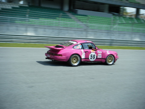 Sepang Afos Pistonheads - The image features a vibrant pink Porsche 911 GT3 driving on a race track. The car's number is 59, visible on the side of the vehicle, indicating its participation in a racing event. The track curve in the background suggests speed and agility, with the driver positioned on the right side of the car, adhering to racing standards.