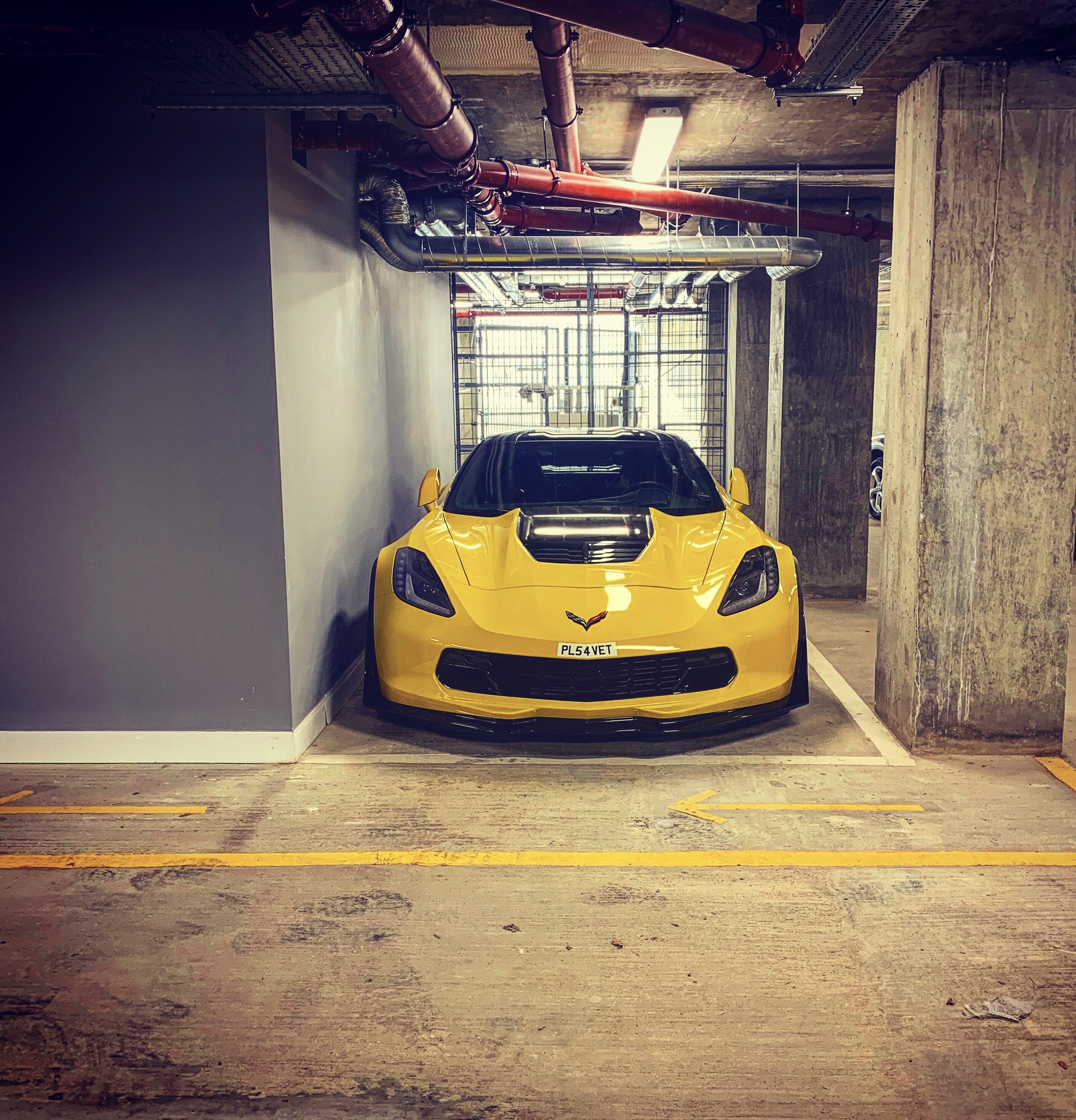 Pistonheads - The image shows a yellow Lamborghini car parked inside a garage. The car is positioned centrally in the frame, with its hood slightly open and its large air intake at the front. The interior of the garage features white walls and a concrete floor, while pipes can be seen running along the ceiling. On the right side of the image, there's a door to the outside world, which is partially visible. The car has a distinctive yellow color and is equipped with a large rear wing. The overall setting suggests that this garage might be a part of a private residence or a specialized storage facility for luxury vehicles.