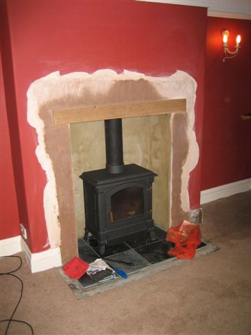 Wood Pro Diy Installing Burner Pistonheads - The image captures a room in the midst of a home renovation. Dominating the room is an old fireplace, its black stove and mantle standing starkly against the vibrant red wall behind it. The wall appears bare and incomplete, suggesting that the renovation is far from finished. The floor, visible on the right side of the image, is made of tiles that are in disarray. In the foreground, various materials and tools of the renovation are scattered haphazardly, indicating the ongoing work taking place.