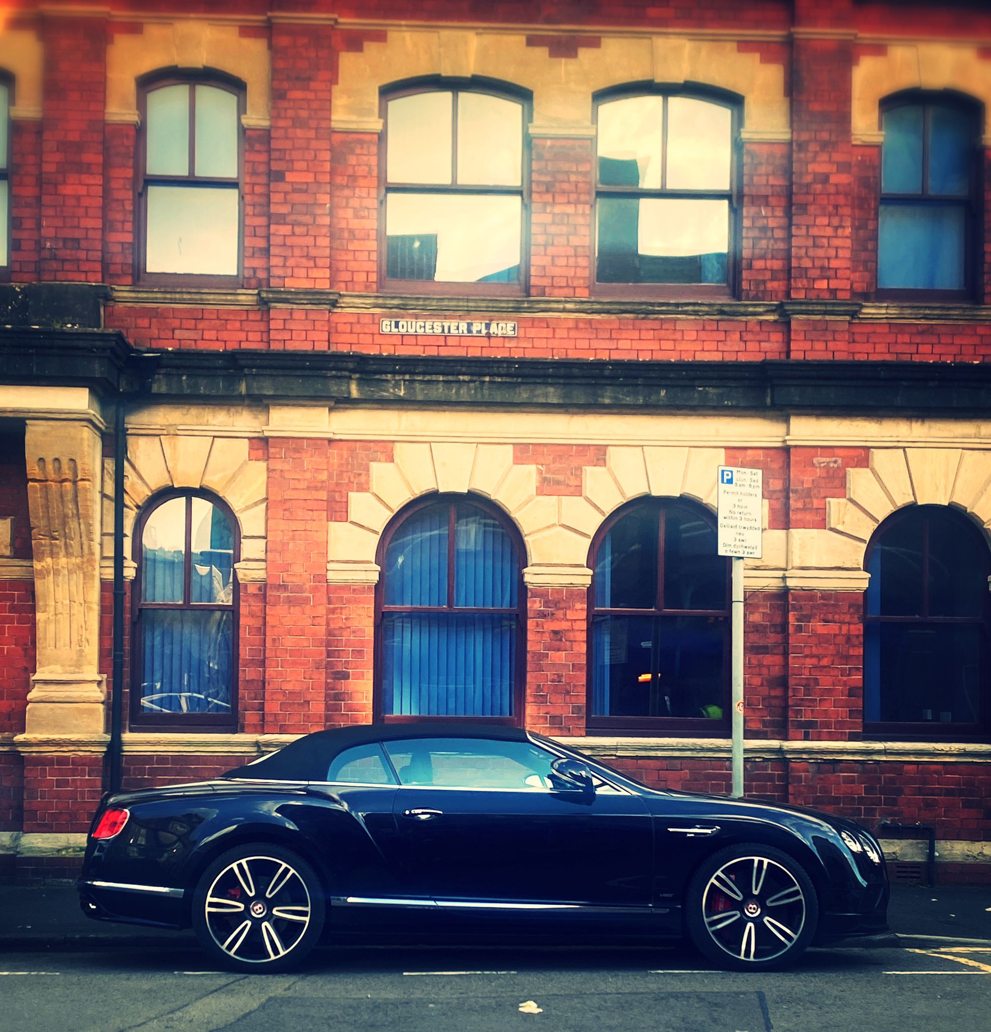 Spotted In South Wales (Vol 3) - Page 374 - South Wales - PistonHeads UK - The image shows a dark blue Bentley parked on the street in front of a brick building. The car is positioned at an angle to the viewer, with its front end visible on the left side of the image and its rear end on the right. The windows are tinted, and the wheels have silver rims with black tires. The building has white window frames and a sign that reads "ELEPHANT LODGE." The sky is overcast, suggesting an overcast or cloudy day. There's no visible activity in the image; it appears to be a quiet moment on the street.