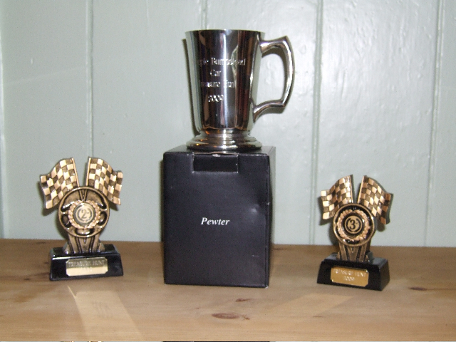 Hunt Treasure July Pistonheads - In the center of the image, there is a black box with the word "Perrier" engraved on it. Atop the black box, there is a silver Perrier pitcher, which appears to be award-winning. To the left and right of the black box, there are two golden trophies. Each trophy has a circular emblem in the middle of it, and around their bases, there are wings. The setting appears to be a ceremony or celebration.